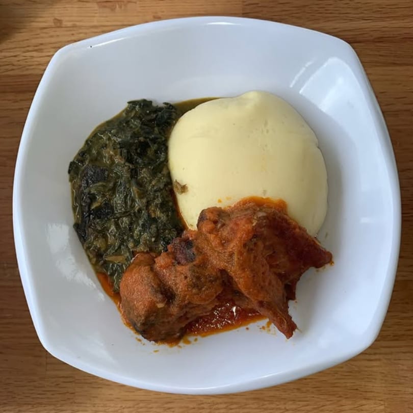 T's Buka African dish with fufu, green stew, and meat in red sauce on a white plate.