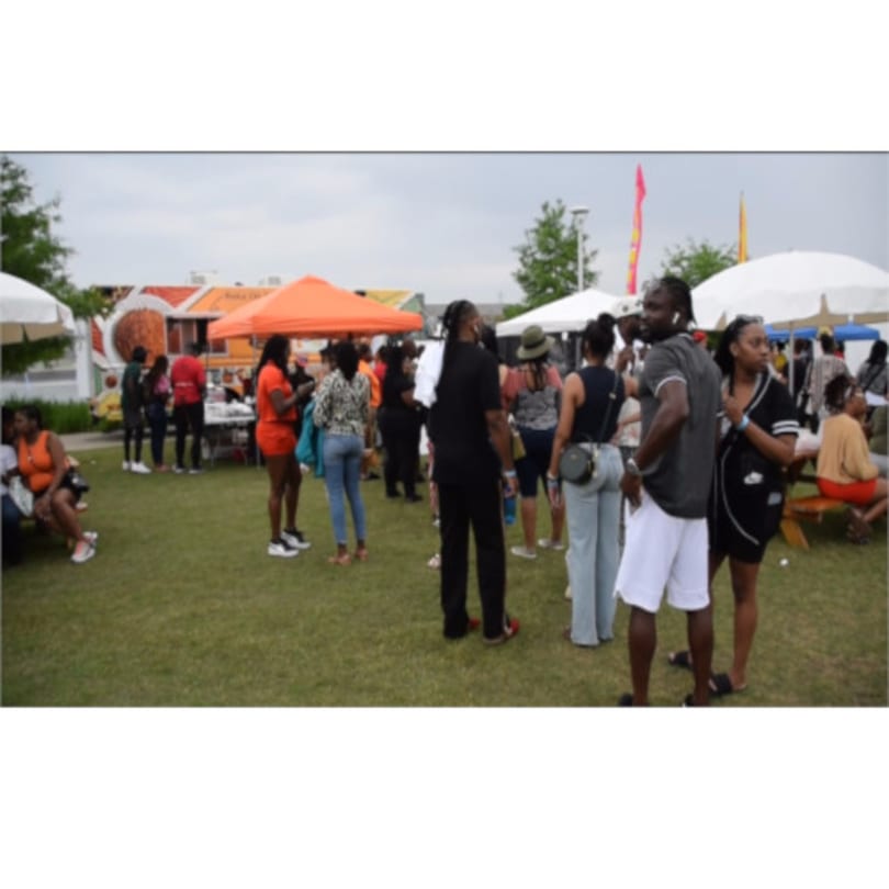 People gather on a grassy field with white and orange tents, enjoying an outdoor event.